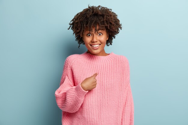 Concept de réaction humaine. Une femme positive à la peau foncée a les cheveux croquants, se montre du doigt, regarde avec plaisir