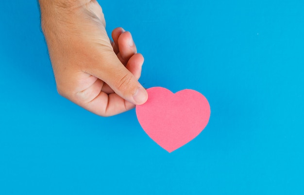 Concept de relation sur table bleue à plat. main tenant le coeur en papier découpé.