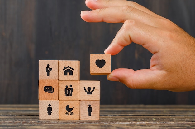 Photo gratuite concept de relation sur la vue de côté de table en bois. main tenant le cube en bois avec l'icône du cœur.