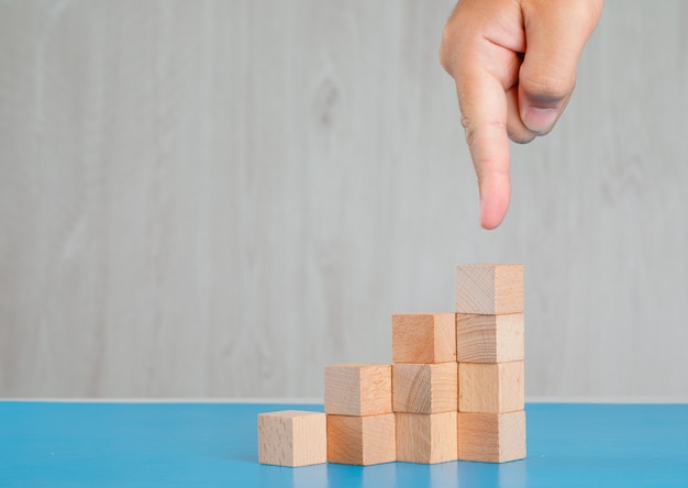 Concept de réussite commerciale sur la vue de côté de table bleue et grise. doigt montrant la pile de cubes en bois.