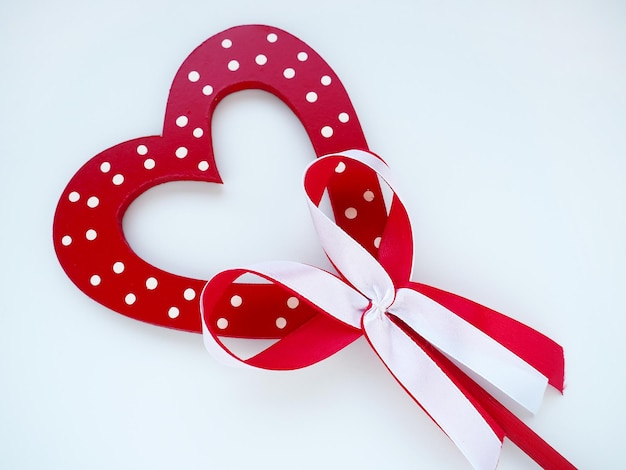 Concept de la saint-valentin. coeur en bois rouge à pois blancs et noeud de ruban sur un bâton. fond blanc. un bel arc comme décoration. amour et relations. reconnaissance ou félicitations