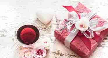 Photo gratuite le concept de la saint-valentin et de la fête des mères, un coffret rouge avec un arc avec des roses et une tasse de thé sur un fond en bois clair