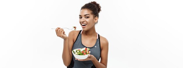 Concept de santé et de remise en forme Belle dame africaine américaine en vêtements de fitness sur le régime alimentaire manger de la salade fraîche isolé sur fond blanc