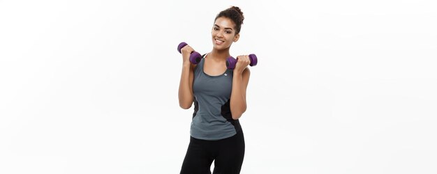 Concept de santé et de remise en forme Belle dame africaine américaine en vêtements de fitness séance d'entraînement avec haltère isolé sur fond blanc