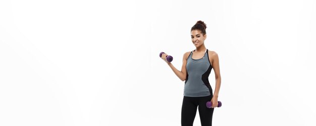 Concept de santé et de remise en forme Pleine longueur de portrait Belle dame africaine américaine en vêtements de fitness gris séance d'entraînement avec haltère isolé sur fond blanc