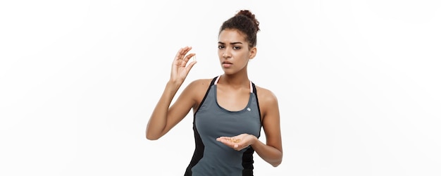 Concept de santé et de remise en forme Portrait en gros plan d'une belle afro-américaine prenant une pilule d'huile de foie de morue isolée sur fond de studio blanc