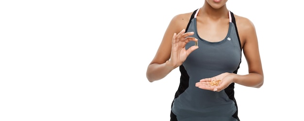 Concept de santé et de remise en forme Portrait en gros plan d'une belle afro-américaine prenant une pilule d'huile de foie de morue isolée sur fond de studio blanc