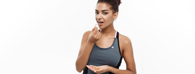 Photo gratuite concept de santé et de remise en forme portrait en gros plan d'une belle afro-américaine prenant une pilule d'huile de foie de morue isolée sur fond de studio blanc