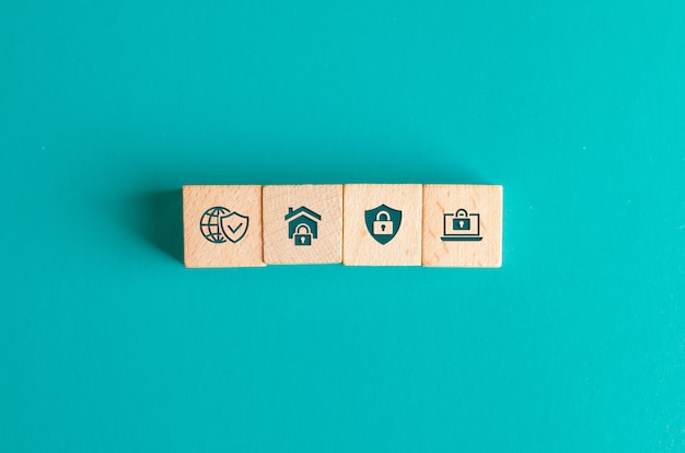 Concept de sécurité avec des icônes sur des blocs de bois sur une table turquoise à plat.