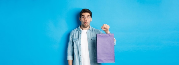 Photo gratuite concept de shopping vacances et style de vie beau mec surpris tenant un sac en papier de la boutique et lo