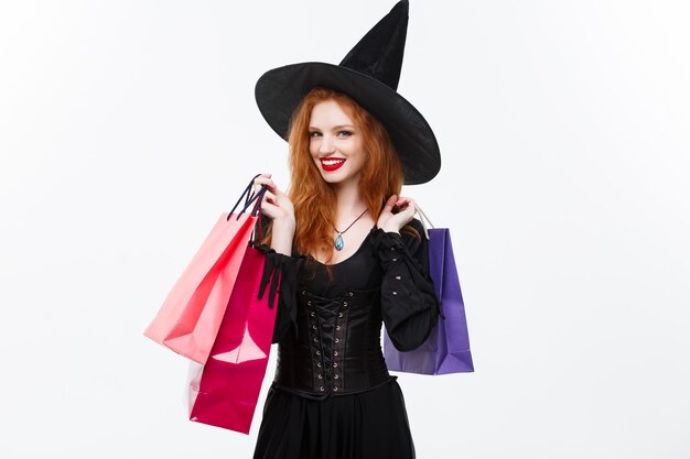 Concept de sorcière d'halloween sorcière d'halloween heureuse souriante et tenant des sacs à provisions colorés sur un mur blanc