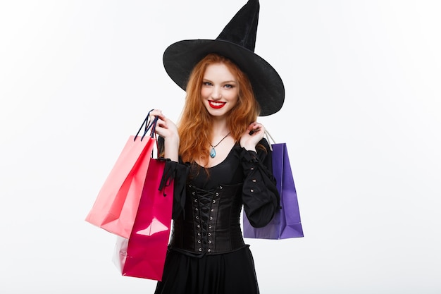 Concept de sorcière d'halloween sorcière d'halloween heureuse souriante et tenant des sacs à provisions colorés sur un mur blanc
