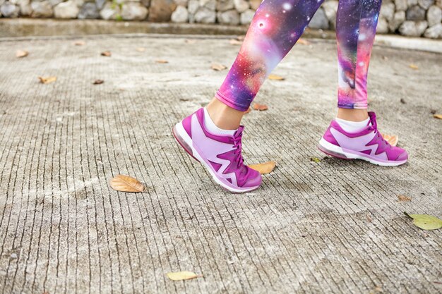 Concept de sport, de remise en forme et de mode de vie sain. Gros coup de pieds féminins en baskets violettes sur le trottoir. Sportive dans l'espace leggings imprimés et chaussures de course élégantes jogging sur route dans le parc