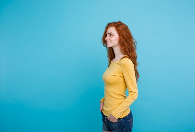 Concept de style de vie - Gros plan Portrait jeune jolie jolie jeune fille aux cheveux roux joue avec ses cheveux avec timidité. Blue Pastel Background. Espace de copie.