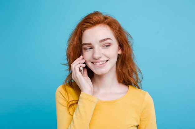 Concept de style de vie et de technologie - Portrait de joyeux joyeux gingembre fille de cheveux roux avec une conversation joyeuse et passionnante avec un ami par téléphone portable. Isolé sur fond bleu pastel. Espace de copie.