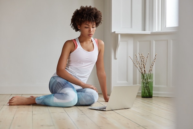 Concept de technologie et de style de vie. Jeune femme noire concentrée regardant une vidéo sur un ordinateur portable