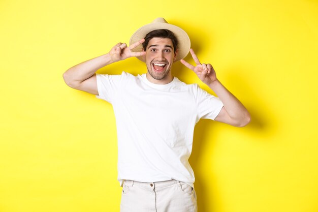 Concept de tourisme et de vacances. Touriste heureux homme posant pour une photo avec des signes de paix, souriant excité, debout sur fond jaune.