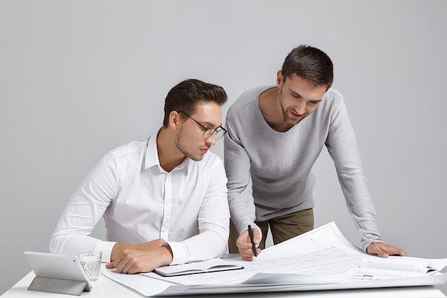 Concept de travail d'équipe, d'emploi et de coopération. Photo de deux jeunes ingénieurs barbus talentueux et enthousiastes travaillant ensemble