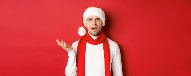 Concept de vacances d'hiver de noël et portrait de célébration d'un homme confus en bonnet et écharpe de santa...