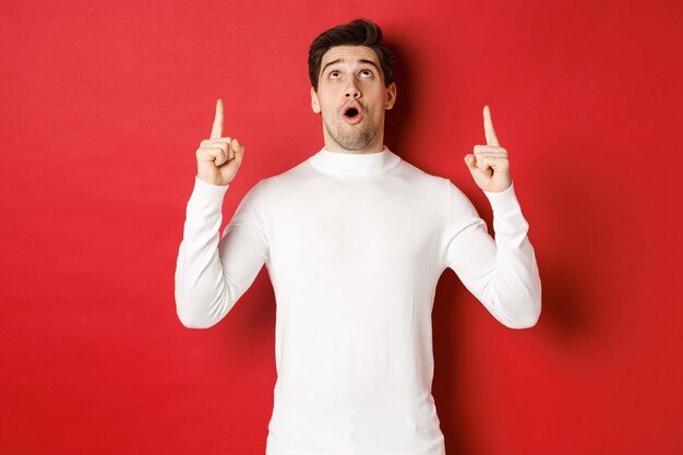 Concept de vacances d'hiver portrait d'un bel homme surpris en pull blanc réagissant au nouvel an ...