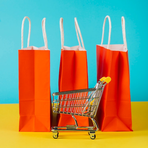 Concept de vente avec chariot devant des sacs à provisions orange