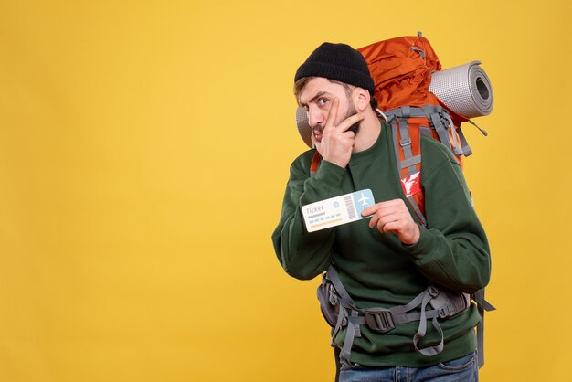 Concept de voyage avec curieux jeune mec avec packpack et billet montrant sur jaune