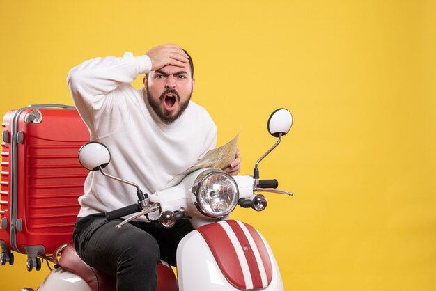 Concept de voyage avec un gars confus assis sur une moto avec une valise dessus tenant une carte en jaune