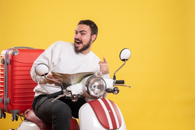 Concept de voyage avec un gars souriant assis sur une moto avec une valise dessus tenant une carte pointant vers l'avant sur jaune