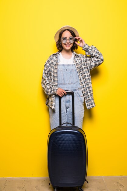 Concept de voyage. Heureuse femme touristique portant chapeau et lunettes de soleil prêt pour le voyage avec valise et passeport isolé.