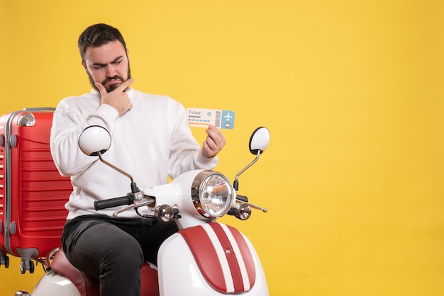 Concept de voyage avec un homme confus assis sur une moto avec une valise dessus montrant un billet en jaune
