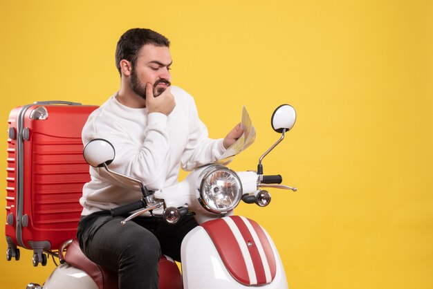 Concept de voyage avec un homme confus assis sur une moto avec une valise dessus tenant une carte en jaune