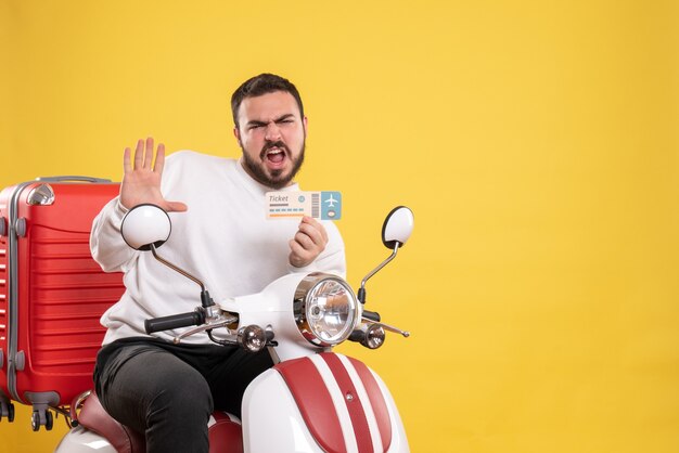 Photo gratuite concept de voyage avec un homme confus émotionnel assis sur une moto avec une valise dessus montrant un billet sur jaune