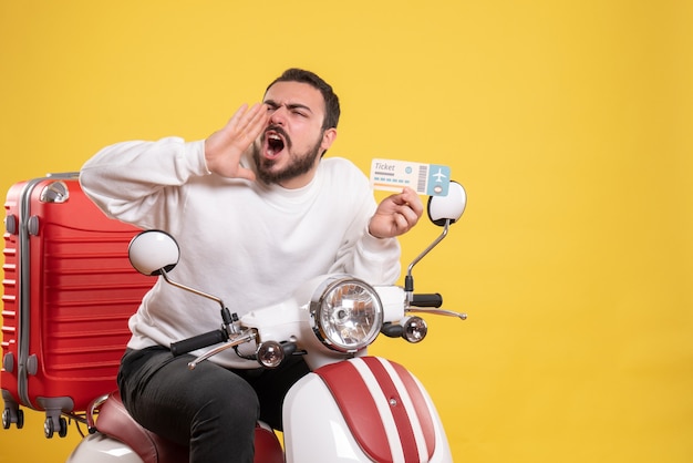 Concept de voyage avec un homme nerveux assis sur une moto avec une valise dessus appelant quelqu'un en jaune