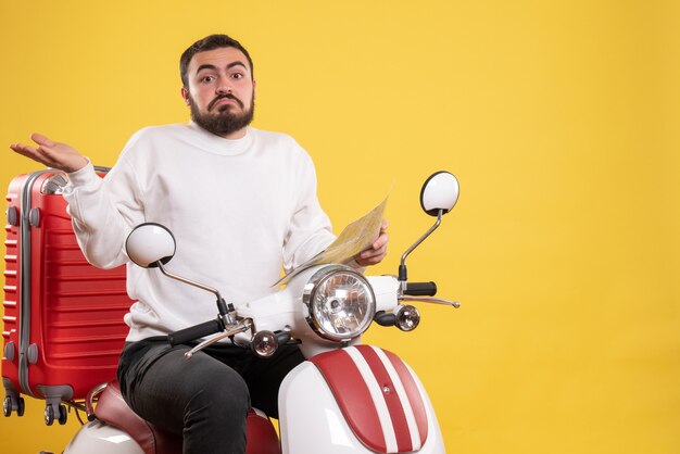 Concept de voyage avec un homme surpris assis sur une moto avec une valise dessus tenant une carte en jaune