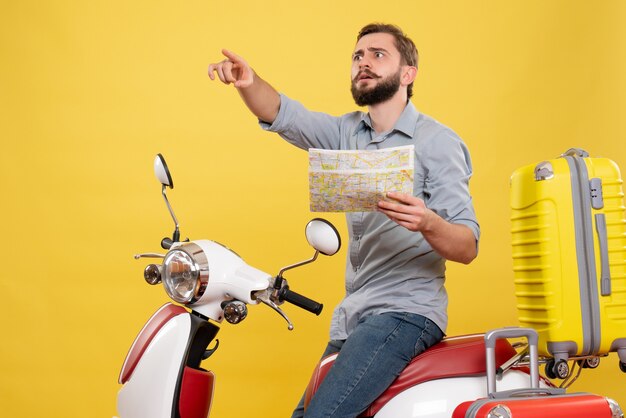 Concept de voyage avec un jeune homme assis sur une moto avec des valises et tenant la carte sur jaune