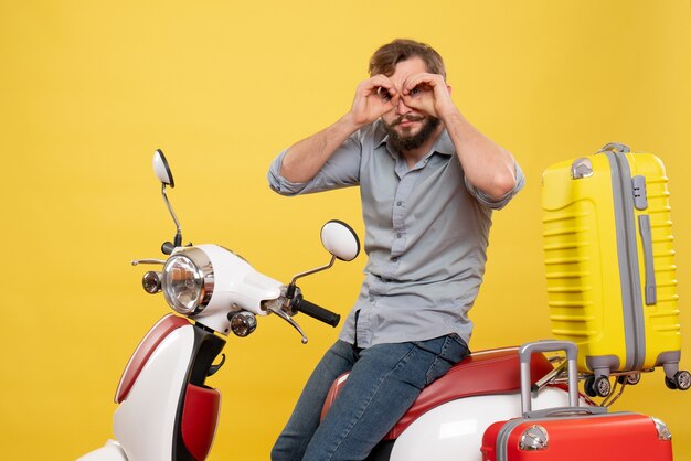 Concept de voyage avec jeune homme barbu émotionnel assis sur la moto sur elle faisant le geste de lunettes sur jaune