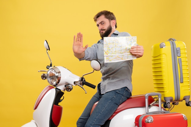 Concept de voyage avec jeune homme barbu émotionnel assis sur la moto et pointant vers l'avant tenant la carte montrant cinq sur elle sur jaune