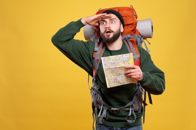 Concept de voyage avec jeune homme choqué avec packpack et tenant la carte sur jaune