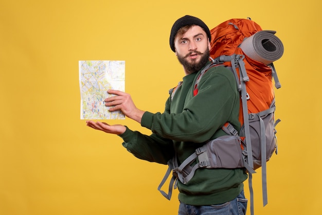 Concept de voyage avec jeune homme concentré avec packpack et tenant la carte sur jaune