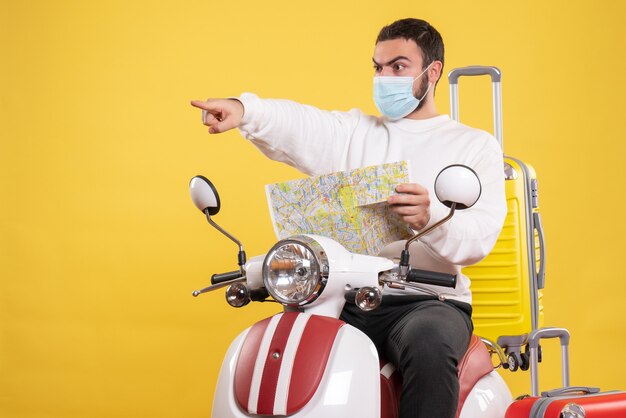 Concept de voyage avec un jeune homme portant un masque médical assis sur une moto avec une valise jaune dessus