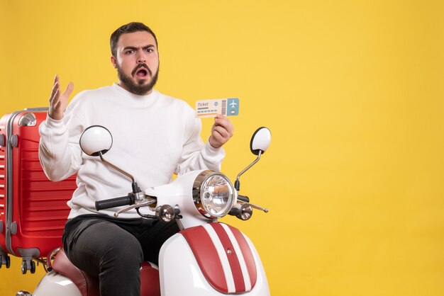 Concept de voyage avec un jeune homme de voyage abasourdi assis sur une moto avec une valise dessus montrant une carte bancaire sur jaune