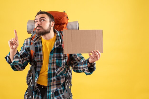 Concept de voyage avec un jeune homme en voyage avec un sac à dos tenant une feuille sans écrire et pointant vers le jaune