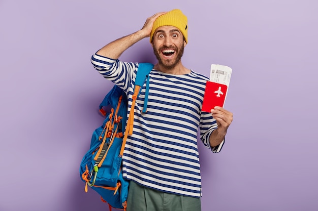 Concept de voyage. Un touriste ravi se réjouit du voyage pendant les vacances d'été pose avec un billet de voyage et des documents organise tout pour le voyage porte un sac à dos. Backpacker a longtemps attendu voyage