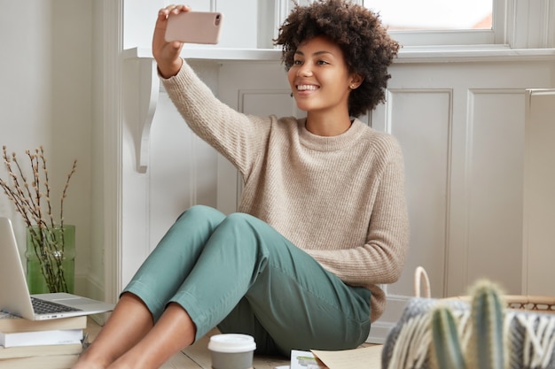 Un concepteur noir joyeux trouve une solution pour réaliser un projet brillant, prend une pause-café, passe un appel vidéo avec un téléphone portable