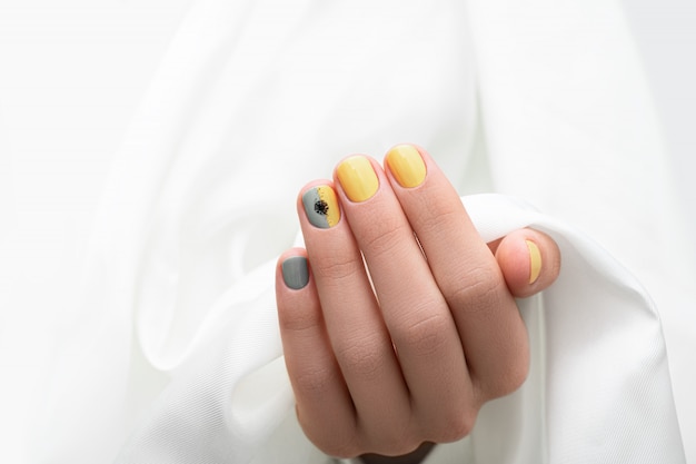 Conception d'ongle jaune et gris. Manucuré main féminine sur fond de tissu blanc.