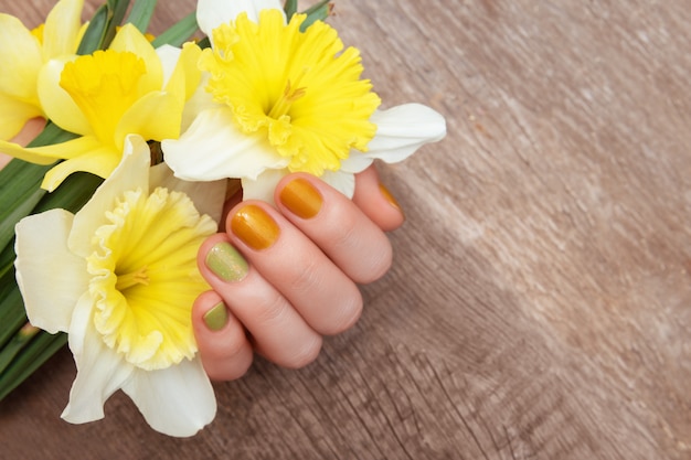 Conception d'ongle jaune. Main féminine avec des paillettes manucure tenant des fleurs de narcisse.