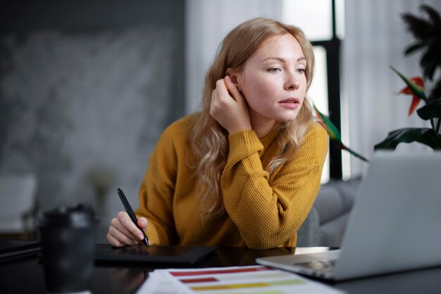 Conceptrice de logo féminin travaillant sur sa tablette connectée à un ordinateur portable