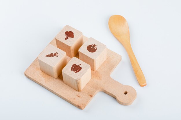 Conceptuel de la cuisine avec des blocs de bois avec des icônes sur la planche de cuisson, cuillère en bois sur table blanche vue grand angle.