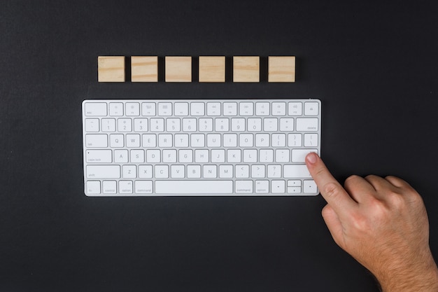 Conceptuel de l'homme de recherche frappant la touche Entrée. avec clavier, cubes en bois sur fond de bureau noir à plat. image horizontale