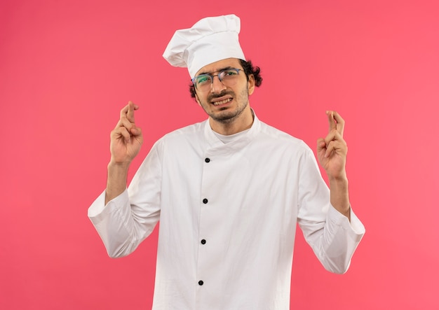 concerné jeune homme cuisinier portant l'uniforme de chef et des lunettes croisant les doigts